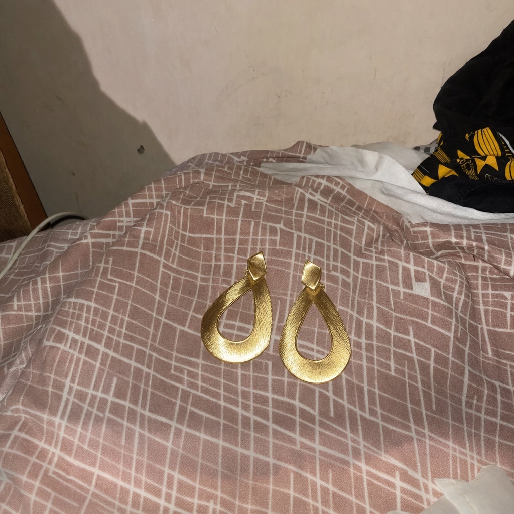 A seller’s phone photo of gold drop earrings on a bedspread
