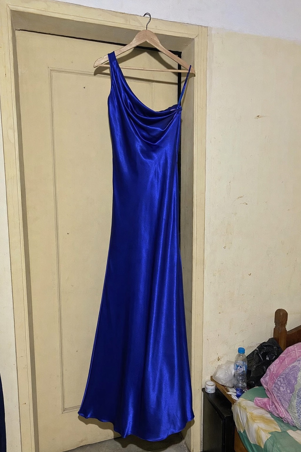 A seller’s phone photo of a cobalt satin gown on a hanger